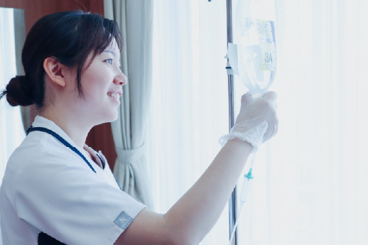白いユニフォームを着用した女性スタッフが、笑顔で点滴の確認や準備を行っている様子