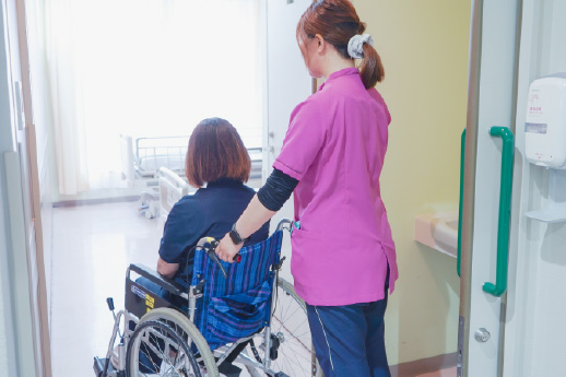 看護師が車椅子の患者を病室へ付き添い、移動を支援している様子