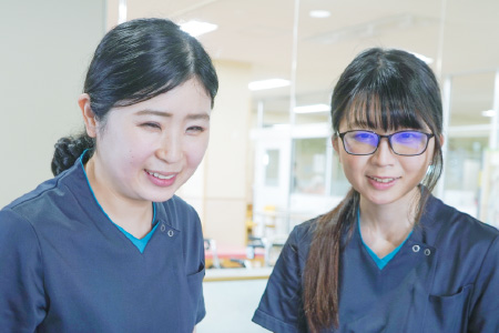 紺色のスクラブを着用した2人の女性スタッフが、笑顔で並んで前方に視線を向けている様子
