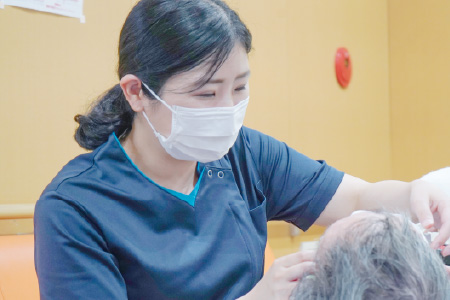 マスクと紺色のスクラブを着用した女性スタッフが、患者の目元や顔まわりのケアを丁寧に行っている様子