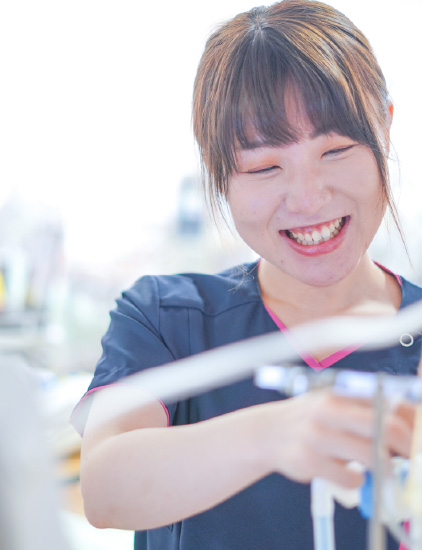 紺色のスクラブを着用した女性スタッフが、親しみやすい笑顔を浮かべながら手元の医療機器を扱っている様子